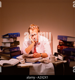 Close-up of an overworked man seated at a desk piled high with books. Stock Photo