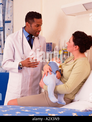 Mother in hospital holding baby boy whilst talking with doctor.