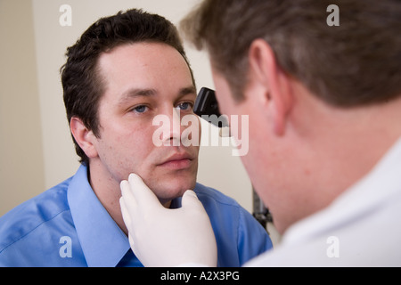 Doctor using a hand held ophthalmoscope to examine the patient's eyes. Stock Photo