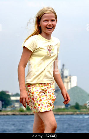 A Pre-Teen blonde girl smiling as she walks along the riverbank. Stock Photo