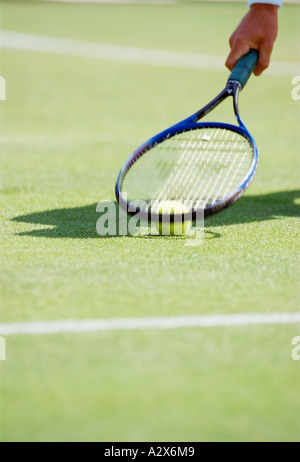 Outdoor close-up of man's hand with tennis racket and ball on grass court. Stock Photo