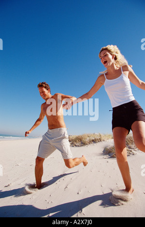 Young couple outdoors at the beach running down sand dune. Stock Photo
