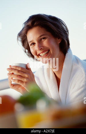 Outdoor portrait of smiling young woman in white robe with hot drink. Stock Photo