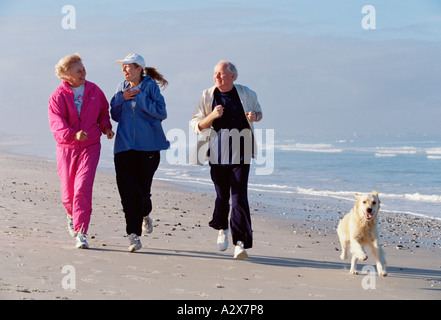 Adult group of three people with their dog running along a beach. Stock Photo