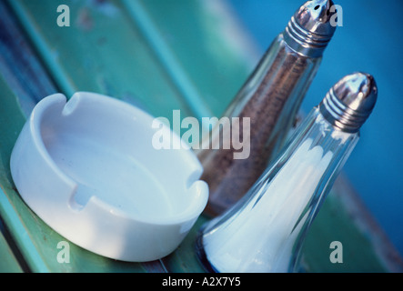 Still life close up of salt and pepper shakers with white ceramic ashtray on outdoor restaurant table. Stock Photo
