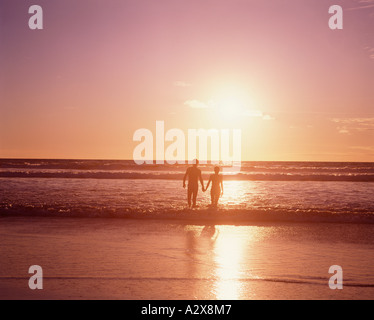 Young couple holding hands at the beach at sunset paddling in the water. Stock Photo