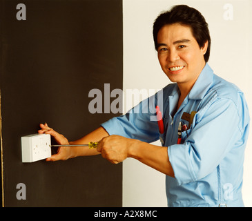 Chinese tradesman electrician demonstrating fitting electrical socket high wall placement. Stock Photo