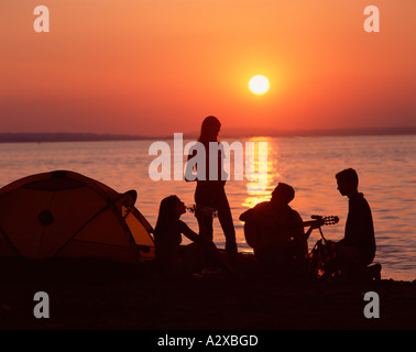 Group of young people camping on a beach at sunset. Stock Photo