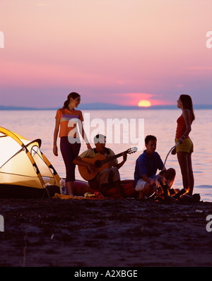 Group of young people camping on a beach at sunset. Stock Photo