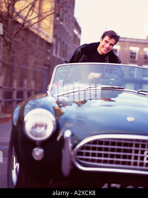Young man with AC Cobra classic sports car in urban street.. Stock Photo