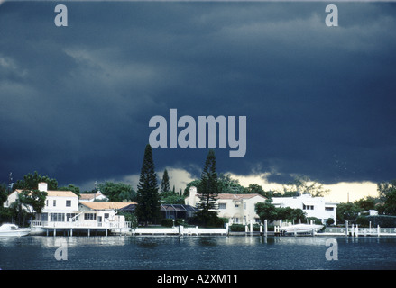 dark heavy clouds hover over elegant expensive looking homes that are next to flat but dark water during a hurricane in miami Stock Photo