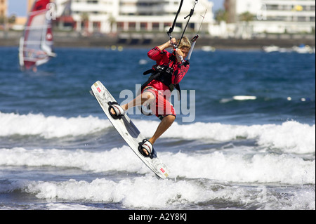 young male kitesurfer in red jumps high off a wave on his board in front of hotels and apartments off El Medano beach Stock Photo