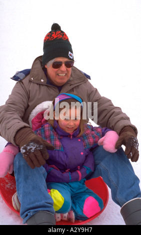 Grandpa sliding down hill with granddaughter age 60 and 4. St Paul Minnesota USA Stock Photo