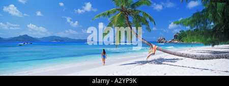 Panoramic scenic of woman at Anse Severe on La Digue Island  with Praslin Island across Indian Ocean Stock Photo