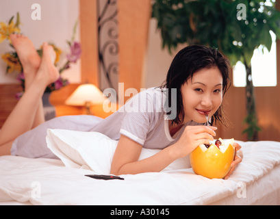 a chinese young woman laying in bed eatting melon Stock Photo