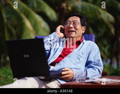a chinese aged man with a laptop and talking on the cell phone Stock Photo