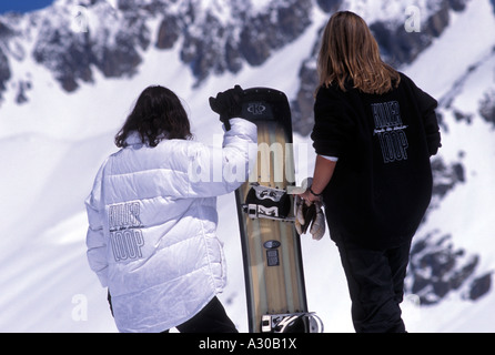 Two female snowboarders walking up the slope with a board Stock Photo