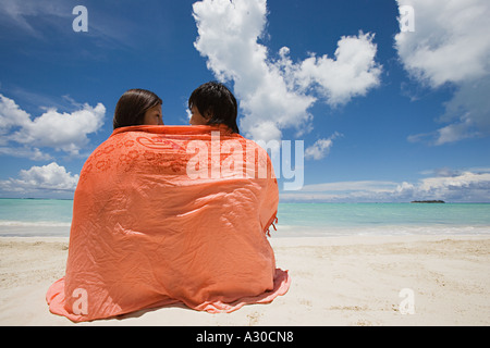 Couple wrapped in shawl on beach Stock Photo
