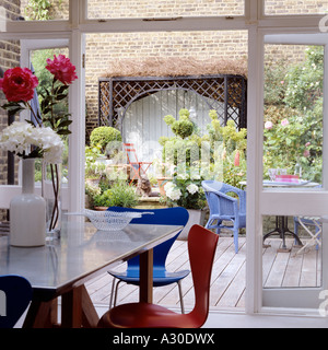 View through open French windows to walled patio with wooden decking, pot plants and boxwood topiary Stock Photo