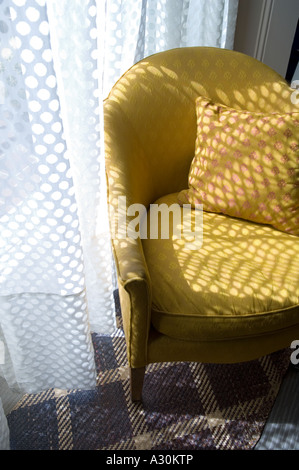 Sunlight dappled on yellow armchair through net curtain Stock Photo