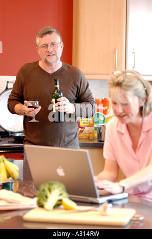 Photograph of a happily married couple preparing lunch and looking online while enjoying a glass of wine at the weekend. Stock Photo