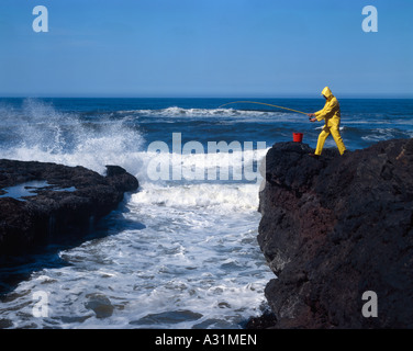 Surf fisherman casting from a steep oceanside cliff into surging waves of the Pacific Ocean in Oregon Stock Photo