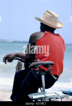 Man wearing a straw hat sitting on bike on beach in Varadero, Cuba Stock Photo