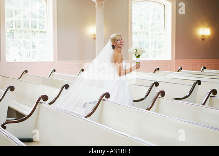 Bride holding wedding bouquet and walking down church aisle Stock Photo