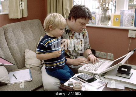 Father doing work on computer at home while tending to his child Stock Photo