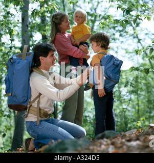 Father adjusting son backpack and mother holding younger child as they prepare to go hiking in the woods Stock Photo