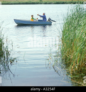 Grandfather holding a stick in his hand and pointing towards the water edge with grandson in hand Stock Photo