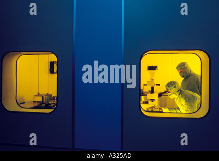 Two lab technicians dressed in protective gear being viewed from the outside in as they work in wafer fabrication Stock Photo