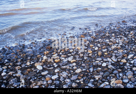 Small waves in a grey sea in warm light breaking onto pebble foreshore Stock Photo