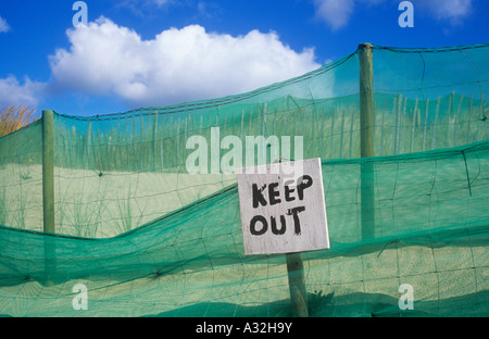 Rough handpainted sign stating Keep out in front of green nylon netting and wire and sheep fencing on sand dunes Stock Photo