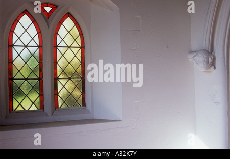 Interior of church porch in warm light with red-fringed diamond leaded windows and worn carved corbel of medieval womans head Stock Photo