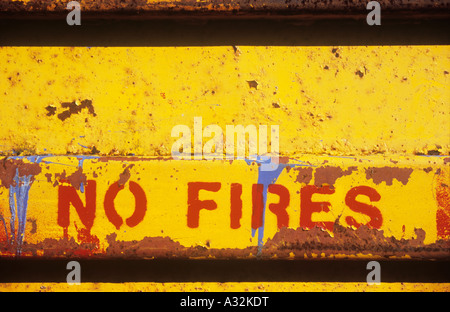 Close up of rubbish skip or bin or dumpster painted yellow with rust scratches and blue paint splashes and red letters No Fires Stock Photo