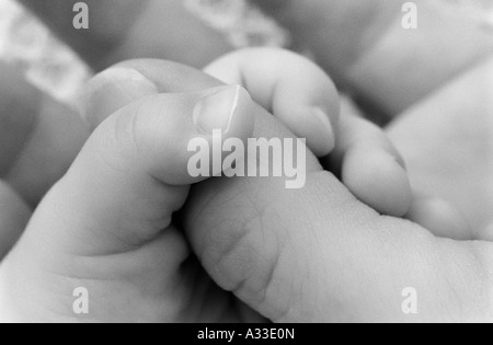 A tiny baby hand grasping an adult thumb. Stock Photo