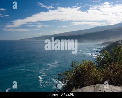Morning mist against dark cliffs with intense blue sea and sky and bright white clouds and surf, Puerto de la Cruz, Tenerife Stock Photo