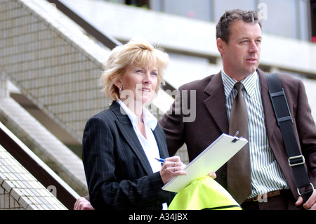British male and female business people on site visit London UK. Surveying building project and making notes on progress. Stock Photo