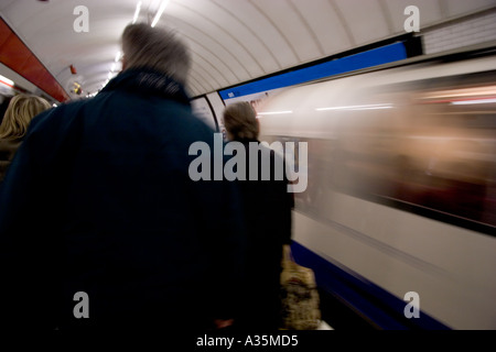 Tube train speeding out of Oxford circus station on the London Underground network with commuters heading towards exit Stock Photo