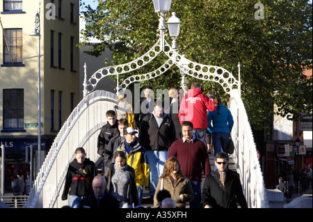 people crossing the hapenny ha penny bridge over the river liffey in dublin at a busy time Stock Photo