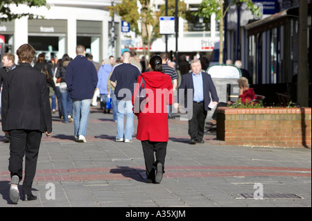 woman in red long coat walks along busy brick paved pedestrian precinct in Belfast City Centre Stock Photo