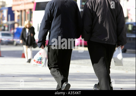 two young businessmen carrying lunch bags walking along footpath on a street in a city centre Stock Photo