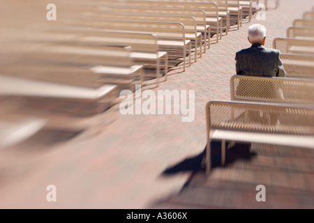 One old man sits alone in the sun among rows of empty benches. Stock Photo