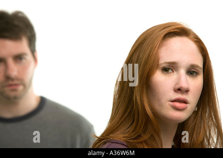 Serious young woman looks at the camera with a man watching her in the background, is she leaving him ? Stock Photo