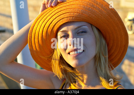 Portrait of a pretty and young Caucasian woman holding her summer hat. Smiling in the sunlight. Stock Photo