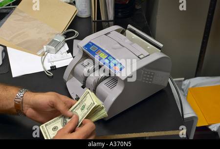Male hands counting US money next to an empty automatic bill counter machine. Stock Photo