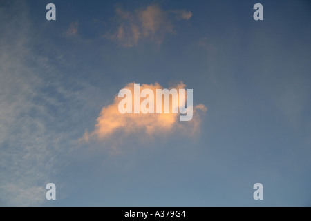 A lone cloud illuminated by the setting sun against a dusk sky. Stock Photo