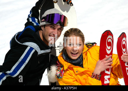 Skifahrerin und Snowboarder, Young Woman in Yellow Ski Dress with Skies and Man with Snowboard in Snow Winter Holiday Stock Photo