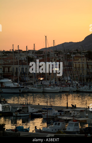 Peach coloured sunrise finds flotilla of white yaghts anchored amongst cruisers & small fishing boats,  Port Aegina, Greece Stock Photo